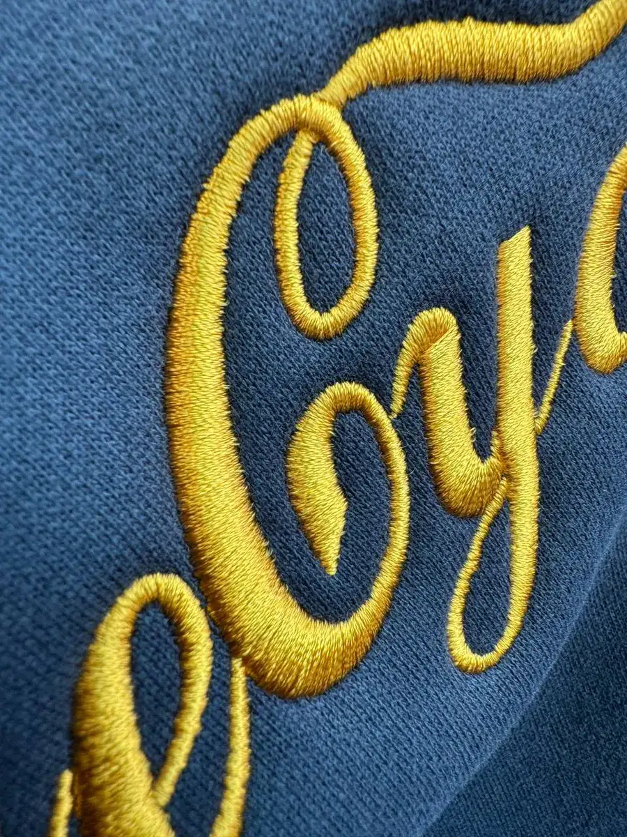 Gold script embroidery on a navy sweatshirt, close up