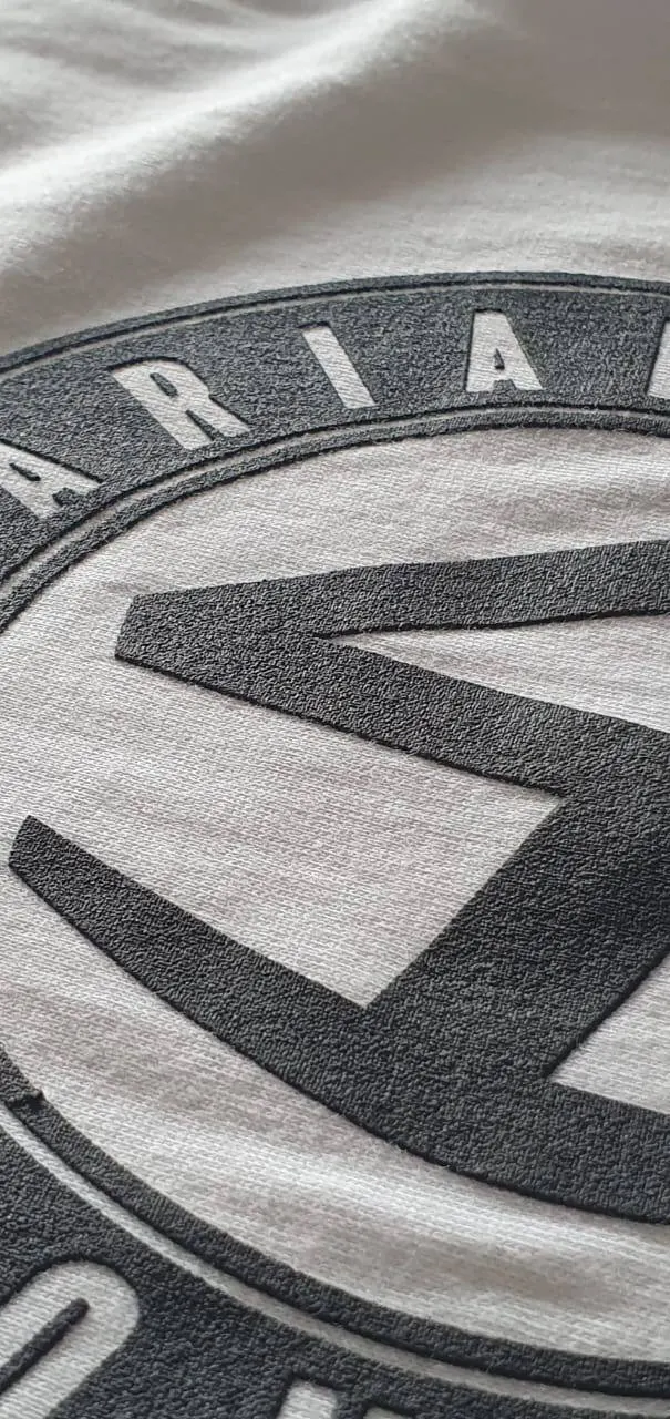 Raised grey emblem print on a white tee, close up